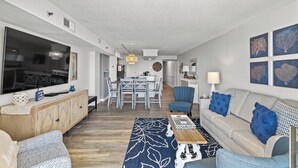 A modern living room with a sofa, coffee table, and a dining area in the background. - Oceans 914 -Oceanfront 2BR- Accommodates 8 (North Myrtle Beach)