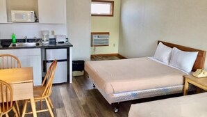 Une chambre d’hôtel de taille réduite, équipée d’une kitchenette, d’un lit, d’un bureau et d’une chaise.