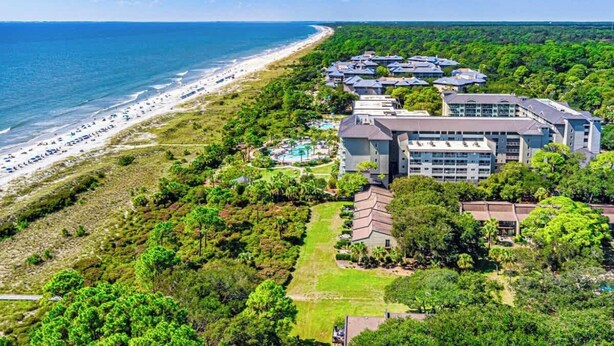 A coastal hotel with multiple buildings, a beach, and lush greenery.