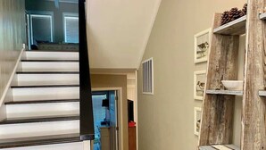 A staircase leading to a room with a door, a wooden shelf with pinecones, and framed pictures on the wall.