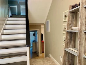 A staircase leading to a room with a door, a wooden shelf with pinecones, and framed pictures on the wall.