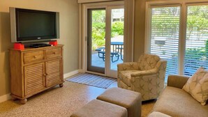 A living room with a TV on a wooden cabinet, a patterned armchair, and a sofa.
