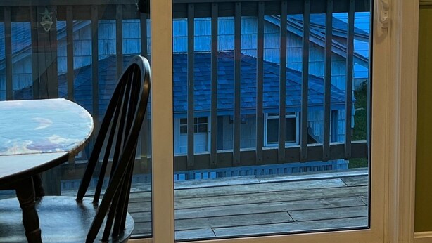 A view from a balcony with a table and chairs, overlooking a body of water and buildings with blue roofs. - ONE MINUTE WALK to WELLS BEACH, Bellevue by the Sea is your perfect vacation! (Wells)