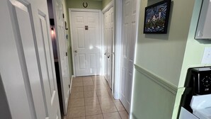 A hallway with white doors, a tiled floor, and a painting on the wall. - ONE MINUTE WALK to WELLS BEACH, Bellevue by the Sea is your perfect vacation! (Wells)