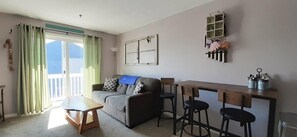 A living room with a sofa, a wooden table, and a bar area with stools.