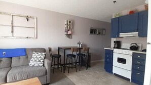 Un espacio habitable compacto con kitchenette, comedor y sofá con cojines estampados.