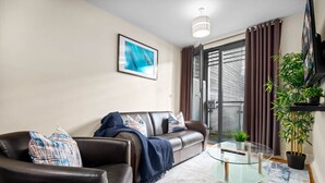 Een moderne woonkamer met een leren bank, een glazen salontafel en een groot raam met gordijnen.