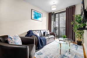 Ein modernes Wohnzimmer mit einer Ledersofa, einem Glastisch und einem großen Fenster mit Vorhängen.