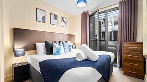 Een moderne hotelkamer met een groot bed, een houten hoofdbord, een nachtkastje, een dressoir en een schuifdeur naar het balkon.