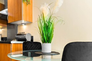 Une cuisine moderne avec une table ronde en verre, un pot de fleurs blanc texturé agrémenté de feuillage vert et de fleurs blanches, et une machine à café noire.