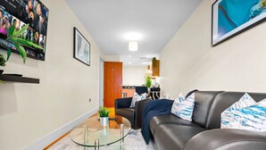 Een moderne woonkamer met een glazen salontafel, een leren bank en een aan de muur bevestigde televisie.