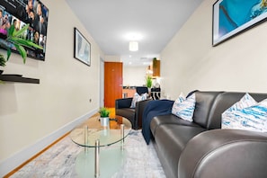 Ein modernes Wohnzimmer mit einem Glastisch, einem Ledersofa und einem an der Wand befestigten Fernseher.