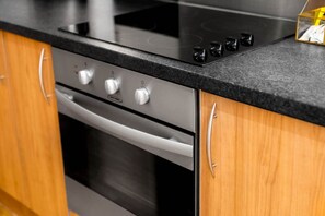 A kitchen with a black countertop, stainless steel oven, and wooden cabinets.