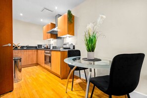 A modern kitchen with wooden cabinets, stainless steel appliances, and a glass dining table with black chairs.