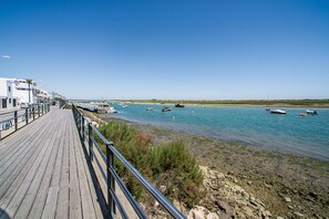 A wooden boardwalk leading to a calm body of water with boats. - Modern & Stylish Apartment in O Pomar Cabanas de Tavira, w/ Pool, Garage & Wifi (Cabanas de Tavira)