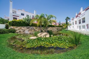 A serene garden with a pond surrounded by lush greenery and a stone wall.