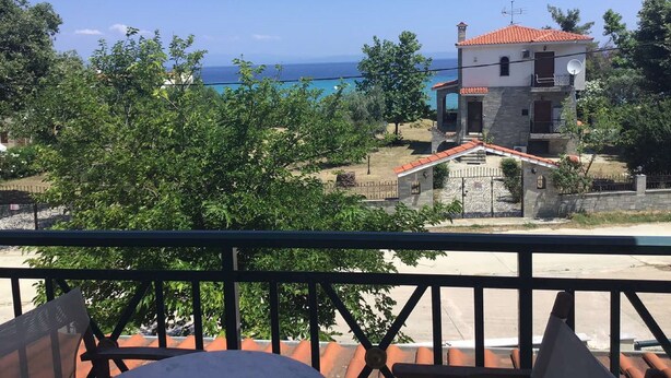 A two-story building with a red-tiled roof, a balcony with a metal railing, and a view of the sea.