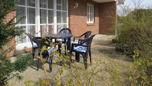 Une terrasse avec une table et des chaises, un bâtiment en briques doté de grandes fenêtres et un petit arbre.