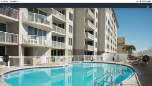 Un espace piscine et jacuzzi avec une piscine d’un bleu éclatant, entouré d’une clôture blanche et d’un immeuble à plusieurs étages doté de balcons.