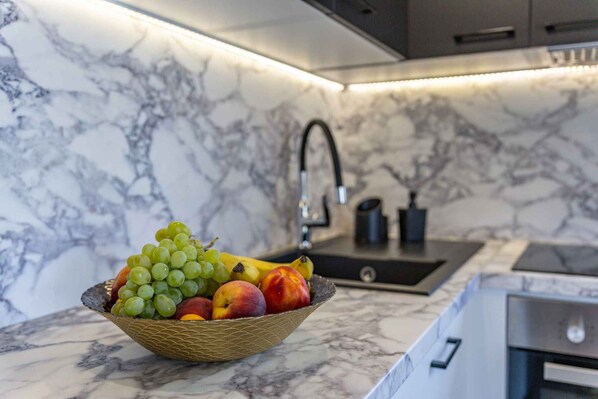 A marble kitchen with a fruit bowl containing grapes, peaches, and bananas on the counter. - Holiday apartment with an open gallery (Malinska)
