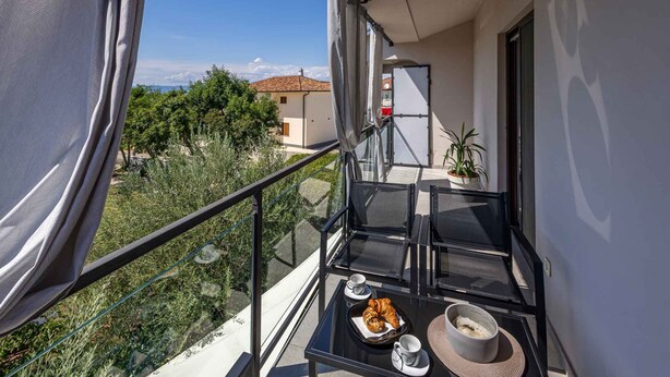 Ein Balkon mit Glastisch, zwei Stühlen, einer Tablett mit Croissants, einer Tasse und einer Schüssel.