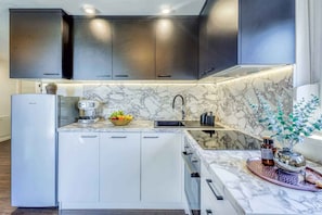 A modern kitchen with marble countertops, a built-in sink, and a refrigerator.