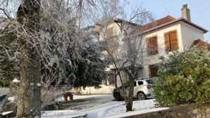 Un quartier résidentiel enneigé, avec une maison, une voiture garée et un mur de pierre.