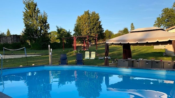 Une piscine d’un bleu éclatant, bordée d’une terrasse en bois, et entourée d’un belvédère et de chaises longues.