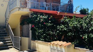 A two-story house with a stone facade, a balcony with metal railings, and a staircase leading to the upper floor. - Villetta 1P NC La Cinta (San Teodoro)