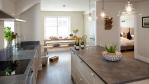 A modern kitchen with a central island, wooden benches, and a dining area in the background.