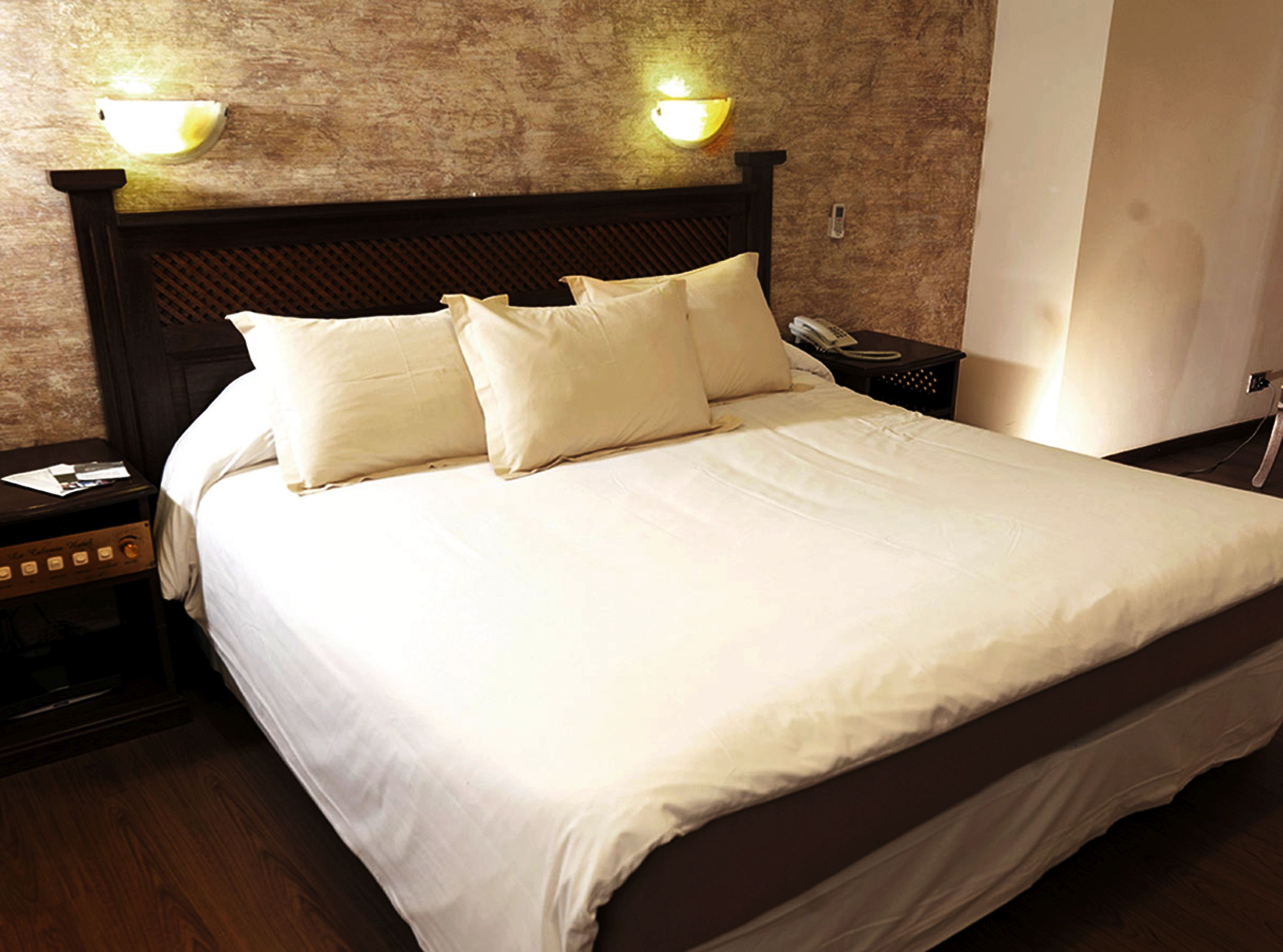 Ein Hotelzimmer mit einem großen Bett, zwei Nachttischlampen, einem Nachttisch und einem hölzernen Kopfteil.