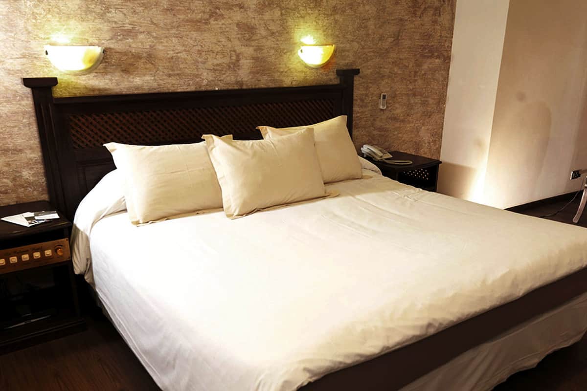 A neatly made bed with white linens and two pillows, a wooden headboard, and bedside lamps.