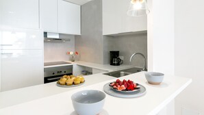 Eine moderne Küche mit weißen Schränken, einer zentralen Kochinsel mit Schüssel und Essensplatten, einer Kaffeemaschine und Pendelleuchten.