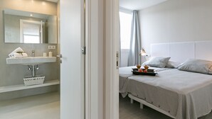Ein modernes Schlafzimmer mit einem großen Bett, einem Nachttisch und einem Badezimmer mit Waschbecken und Spiegel.