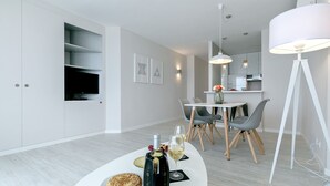 Ein modernes Wohnzimmer mit Essbereich, weißen Möbeln, einer Weinflasche und Gläsern auf einem Tisch.