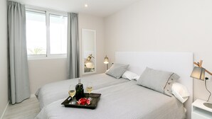 A modern hotel room with a large bed, a bedside table, a nightstand, a lamp, and a window with curtains. - Nice beachfront apartment in Puerto Pollensa (Port de Pollença)