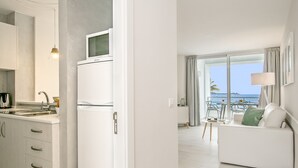 A modern kitchen with a refrigerator, a sink, and a dining area with a white sofa and a table. - Nice beachfront apartment in Puerto Pollensa (Port de Pollença)