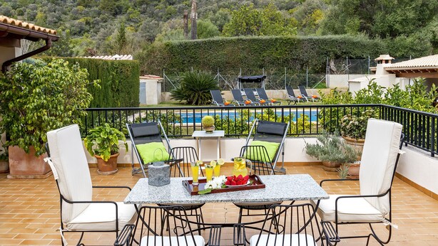 Una terraza con una mesa, sillas y vistas a una piscina y árboles.
