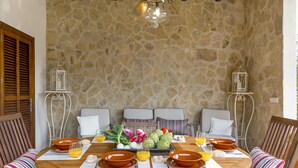 Comedor con pared de piedra y una mesa redonda dispuesta para seis personas, rodeada de sillas con cojines.