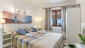 Una camera da letto ordinata con un letto, cuscini, un comodino e un quadro raffigurante un faro.