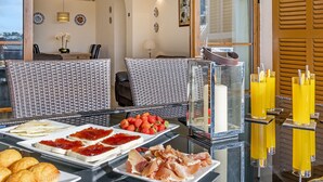 A breakfast buffet with various food items, wicker chairs, and a glass table with a view of the outside. - 1st line apartment in Alcudia Beach CAR (Alcúdia)