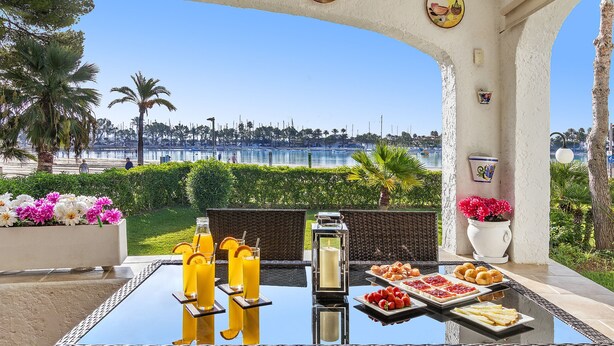 A table with drinks and food, a view of the sea, palm trees, and a beach. - 1st line apartment in Alcudia Beach CAR (Alcúdia)