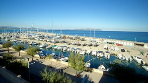 Marina com vários barcos atracados, céu claro e uma cordilheira ao longe.