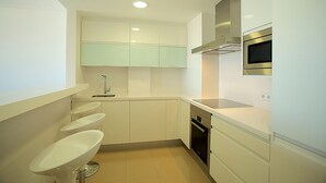 Uma cozinha moderna com armários brancos, forno de aço inoxidável e micro-ondas embutido.
