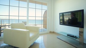 Uma sala de estar moderna com uma televisão grande, um sofá branco e uma mesa de centro de vidro.