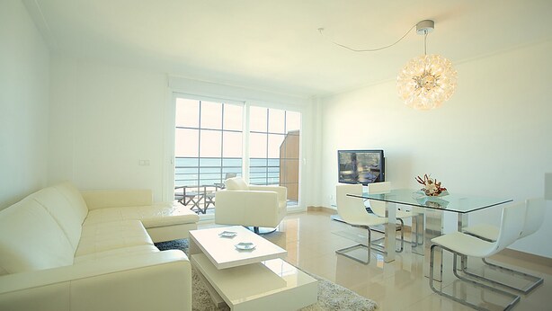 Uma sala de estar moderna com sofá branco, mesa de centro de vidro e um espaço de jantar com mesa e cadeiras de vidro.