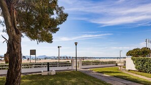 A park with a pathway, a tree, and a view of the beach. - Seafront apartment in Alcudia beach (Port d´Alcudia)