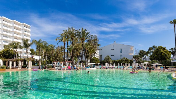 A swimming pool with clear water, surrounded by palm trees and lounge chairs. - Seafront apartment in Alcudia beach (Port d´Alcudia)