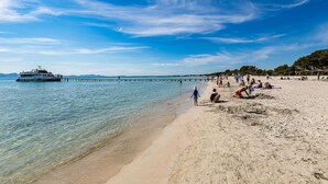 A beach with clear water, a pier, and people relaxing on the sand. - Seafront apartment in Alcudia beach (Port d´Alcudia)