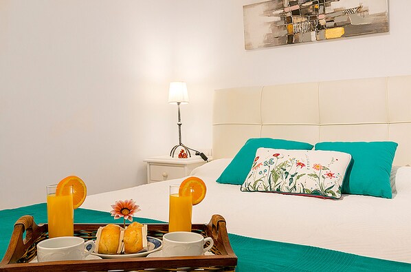A neatly made bed with teal bedding, a bedside table with a lamp, and a tray with breakfast items. - Seafront apartment in Alcudia beach (Port d´Alcudia)